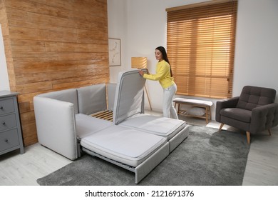 Young woman unfolding sofa into a bed in room. Modern interior