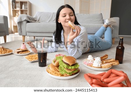 Young woman with unhealthy food lying on floor at home. Overeating concept
