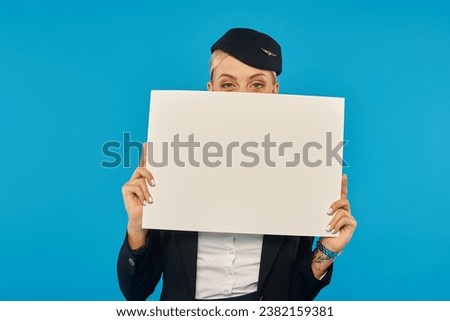 young woman in uniform of flight attendant obscuring face with blank placard on blue background