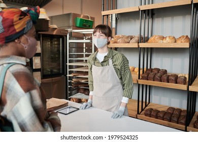 Young Woman In Uniform And In Mask Selling Bread To The Customer In Bakery Shop