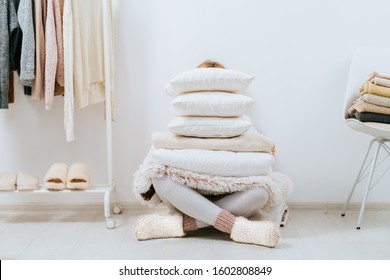 Young woman unrecognizable housewife sitting on floor holding a stack of pillows, cover plaid on white wall stack tower design in scandinavian style, clothes rack in modern light empty wardrobe room. - Shutterstock ID 1602808849