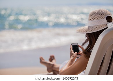 Young woman updating her social network status while relaxing at the beach