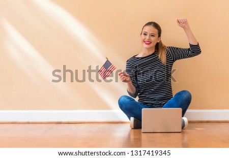 Young woman with USA flag using a laptop computer against a big interior wall