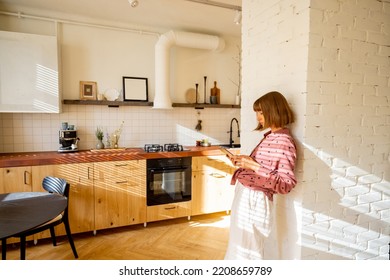 Young Woman Use Digital Tablet While Standing In Bright And Sunny Studio Apartment. Work Online Or Having Leisure Time With Digital Devices At Home