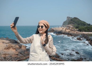 A young woman uses her smartphone to take a picture of the beautiful coastal scenery at Yehliu Geopark in Taiwan. Taking in the beauty of nature while fusing themes of tourism, adventure, and travel - Powered by Shutterstock