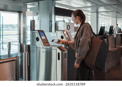 A young woman uses her smartphone to scan a boarding pass at an automated airport gate. Concept of digitalization, self-check-in and independent travel.