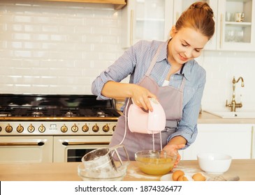 Young woman uses mixer in beating eggs, stands in a modern kitchen