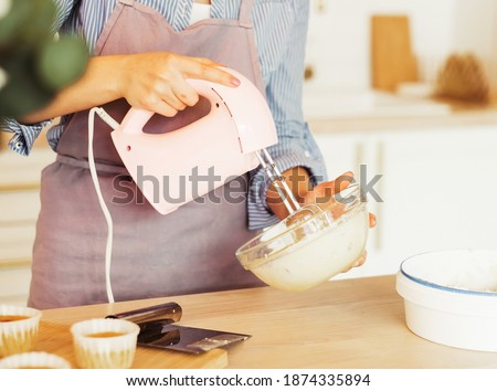 Young woman uses mixer and whips cream for cake, stands in modern kitchen