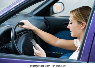 Young woman using cell phone while driving car