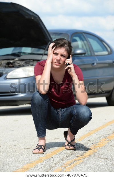 Young woman using cellphone to call for\
road assistance with broken car in\
background
