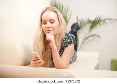 young woman using cellphone while lying on couch at home