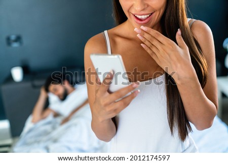 Young woman using cellphone while her husband sleeping on bed
