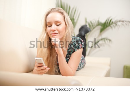 young woman using cellphone while lying on couch at home