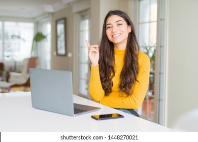 Young woman using computer laptop with a big smile on face, pointing with hand and finger to the side looking at the camera. - Shutterstock ID 1448270021
