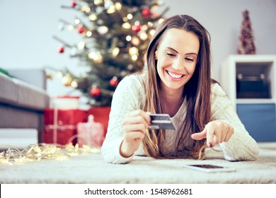 Young Woman Using Credit Card And Phone To Pay For Christmas Shopping