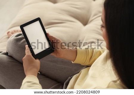 Young woman using e-book reader on sofa, closeup