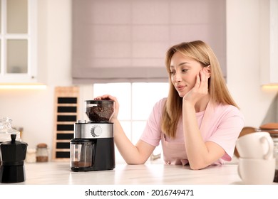 Young woman using electric coffee grinder in kitchen