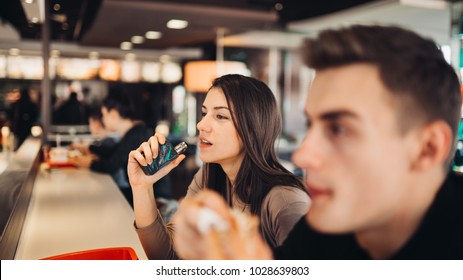 Young woman using electronic cigarette to smoke in public places.Smoke restriction,smoking ban.Using vaping device with flavoured liquid.E-juice vaping.Smoking habit,nicotine addict,tobacco industry