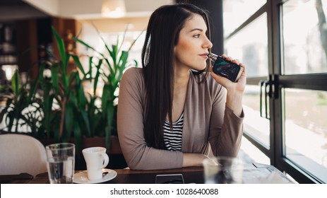 Young Woman Using Electronic Cigarette To Smoke In Public Places.Smoke Restriction,smoking Ban.Using Vaping Device With Flavoured Liquid.E-juice Vaping.Smoking Habit,nicotine Addict,tobacco Industry