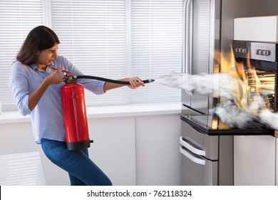Young Woman Using Fire Extinguisher To Put Out Fire From Oven At Home