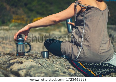 A young woman is using a french press to make coffee outdoors in nature