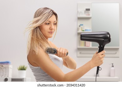 Young woman using a hairbrush and a blowdrying hair in a bathroom 
