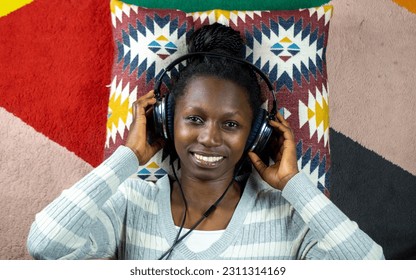 young woman using headphones while lying on a colorful carpet  - Shutterstock ID 2311314169
