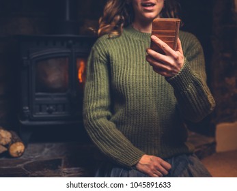 A Young Woman Is Using Her Smart Phone By The Fire Of A Log Burner