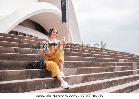 Young woman using her smartphone sitting outdoors on the stairs and using social networks. Concept: lifestyle, outdoors, freedom