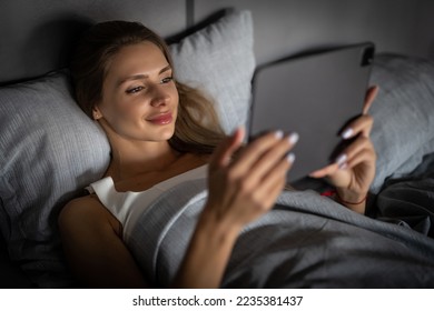 Young woman using her tablet computer in her bed late at night - Powered by Shutterstock