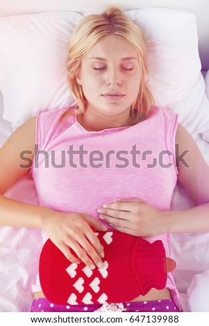Young woman using hot water bottle on abdomen while lying on bed