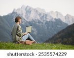 Young woman using laptop computer in mountains. Girl freelancer working outdoor. Freelance work, travel, vacations, stay connected, communication, studying online, e-learning concept