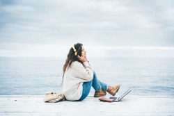 Young Woman Using Laptop Computer And Listening Music Near Winter Sea. Freelance Work Concept