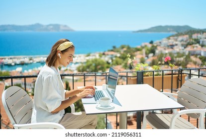 Young woman using laptop computer at cafe balcony of resort hotel with sea view, working typing emails browsing online enjoying drinking coffee - Powered by Shutterstock