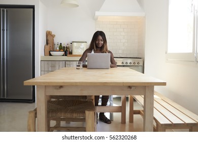 Young Woman Using Laptop Computer In Her Kitchen, Front View