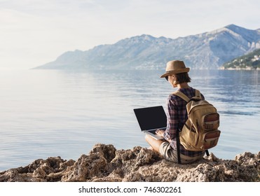 Young Woman Using Laptop Computer By Sea. Freelance Work Concept. People Using Devices To Plan Trips, Check In To Hotels And Flights, Stay Connected To Family And Office From Remote Part Of The World