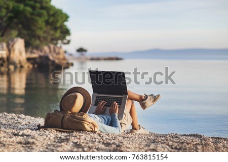 Young woman using laptop computer on a beach. Girl freelancer working by the sea. Freelance work, travel, vacations, stay connected, communication, studying online, e-learning concept
