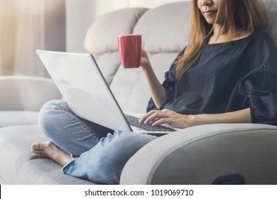 Young Woman Using Laptop And Drinking Cofee On Sofa At Home