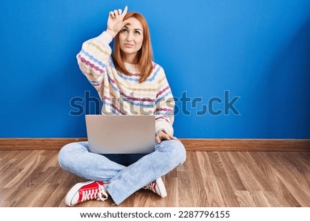 Young woman using laptop at home sitting on the floor making fun of people with fingers on forehead doing loser gesture mocking and insulting. 