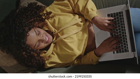 Young Woman Using Laptop Looking Up To Camera Smiling. From Above Angle Of Girl Face Using Computer On Couch. A Relaxed Brazilian Person Browsing Internet On Modern Technological Device