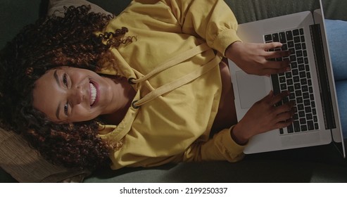 Young Woman Using Laptop Looking Up To Camera Smiling. From Above Angle Of Girl Face Using Computer On Couch. A Relaxed Brazilian Person Browsing Internet On Modern Technological Device