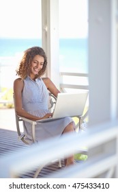 Young Woman Using Laptop On Beach House Balcony