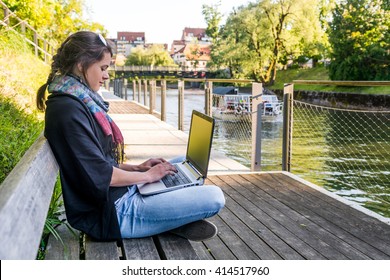 Young woman using laptop at a riverbank.