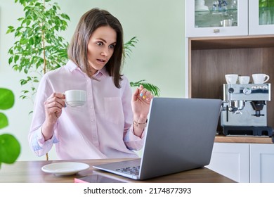 Young Woman Using Laptop Sitting In Kitchen At Home