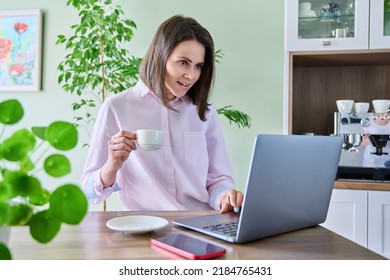 Young Woman Using Laptop Sitting In Kitchen At Home