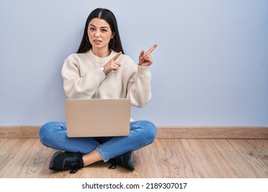 Young Woman Using Laptop Sitting On The Floor At Home Pointing Aside Worried And Nervous With Both Hands, Concerned And Surprised Expression 