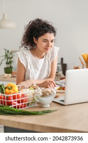 Young Woman Using Laptop While Eating In Kitchen