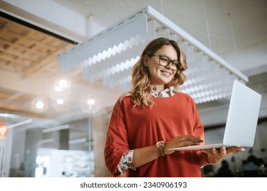 Young woman using a laptop while working in a startup company office - Powered by Shutterstock