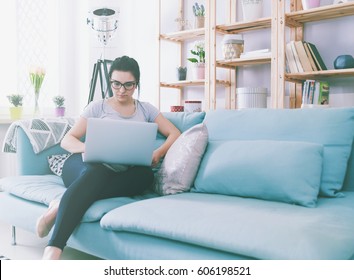 Young woman using laptop while sitting on comfortable sofa, home interior - Shutterstock ID 606198521