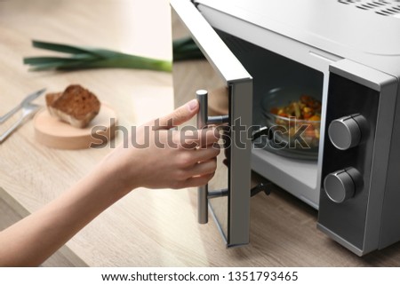Young woman using microwave oven on table in kitchen